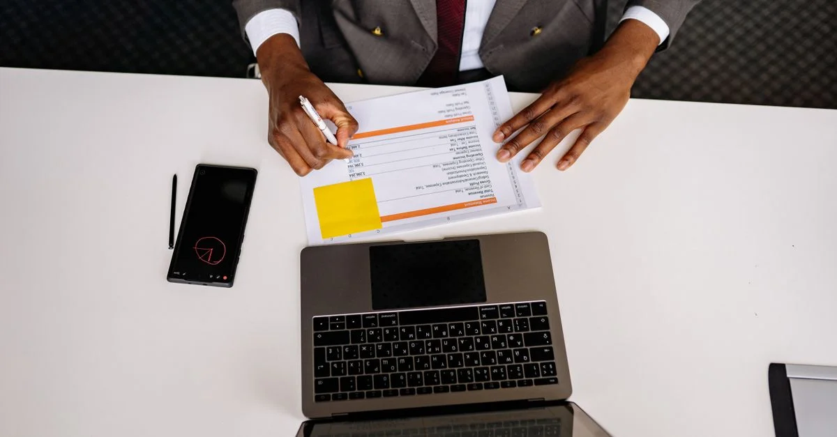Vue de dessus d'un professionnel des affaires analysant des documents avec un ordinateur portable sur un bureau blanc dans un cadre de bureau.