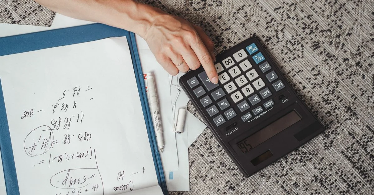 Vue de dessus d'une main calculant des chiffres avec une grande calculatrice et des notes sur un bureau.