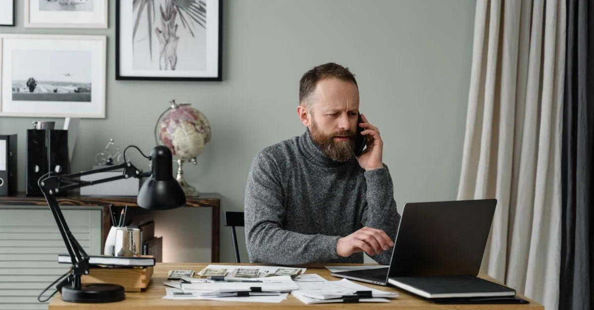 Homme barbu multitâchant avec un ordinateur portable et un téléphone à un bureau de bureau moderne