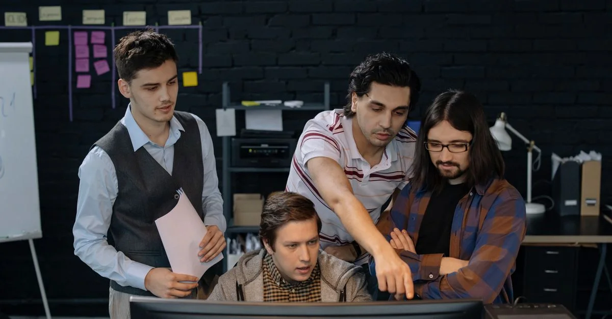 Groupe de professionnels discutant d'un projet à un ordinateur dans un environnement de bureau moderne.