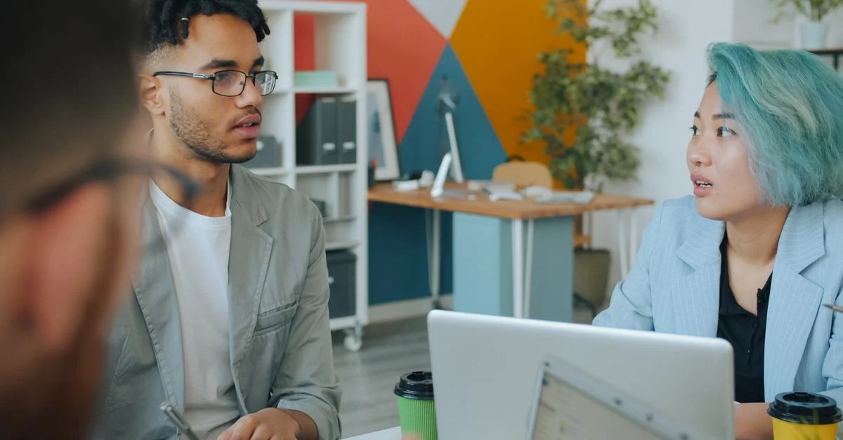Des collègues de différentes origines ethniques discutent d'idées dans un environnement de bureau moderne, favorisant la collaboration et l'innovation.