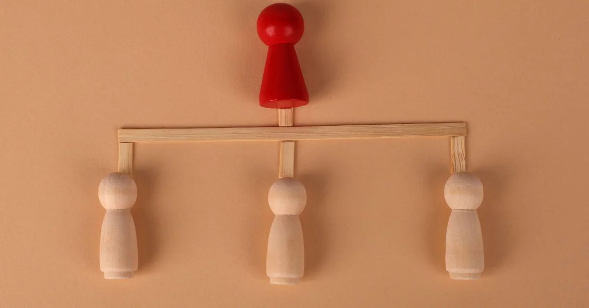 Agencement minimaliste de figurines en bois représentant la hiérarchie et le concept de leadership.