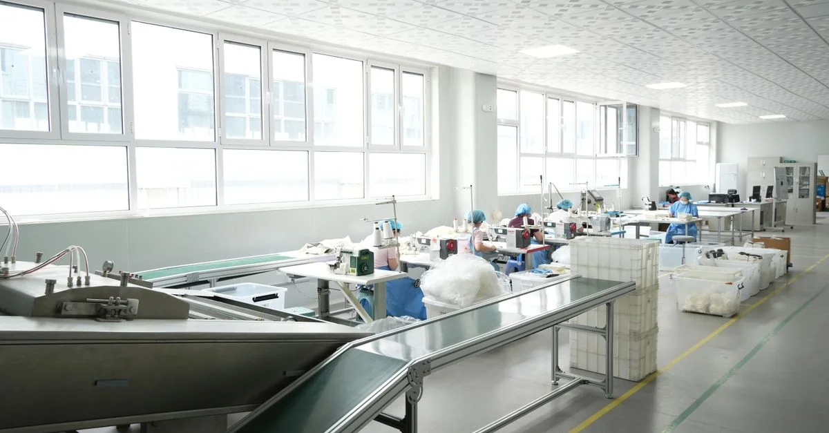 L'intérieur d'une usine moderne, avec des ouvriers qui font fonctionner des machines à coudre sous un éclairage vif.