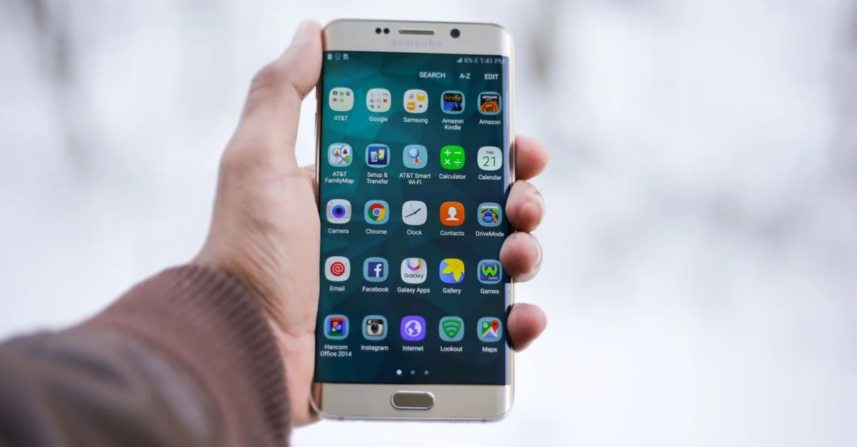 Gros plan sur une main tenant un smartphone Samsung affichant diverses icônes d'applications, mettant l'accent sur la technologie et la connectivité.