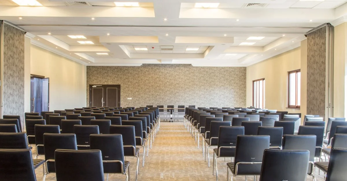 Salle de conférence spacieuse et vide avec un design moderne et des chaises noires soigneusement disposées.