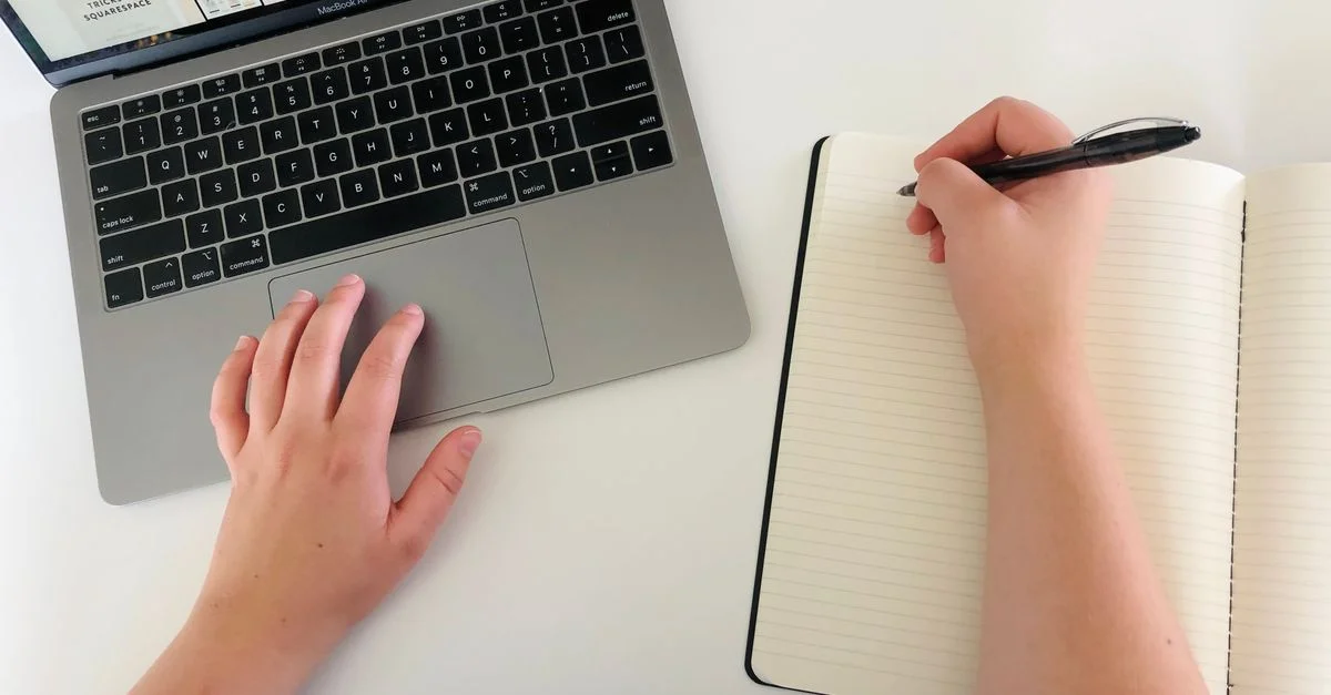 Vue de dessus d'une femme travaillant à distance avec un ordinateur portable et un notebook, mettant en valeur la productivité et le multitâche.