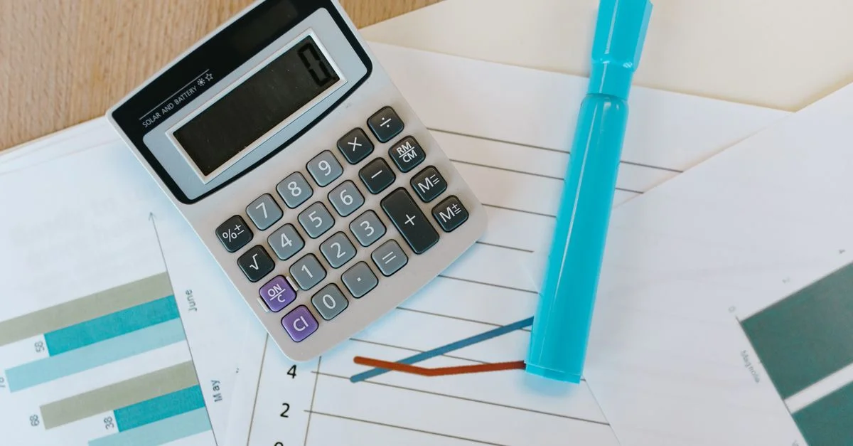 Vue de dessus d'une calculatrice et de graphiques sur un bureau en bois avec un marqueur bleu.